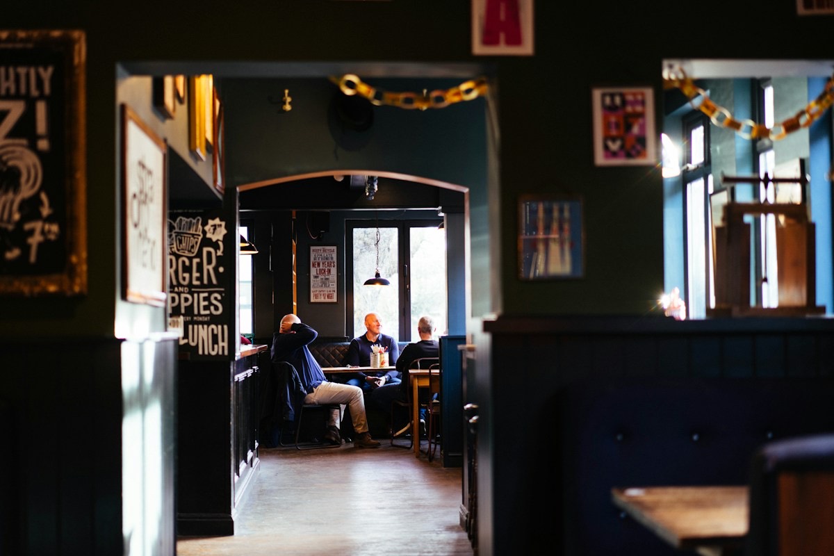 Gjester ved et bord inne på en mørk pub med grønne vegger og en lampe over bordet